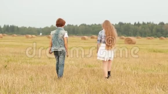十几岁的女孩和男孩在干草堆背景下的收割场上散步快乐的女孩和男孩在乡下玩视频的预览图