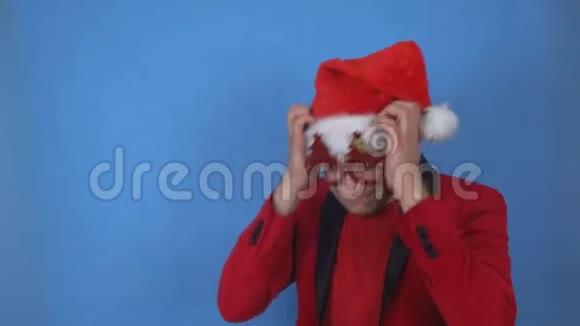 穿着圣诞老人服装的年轻人抱着他的头在蓝色背景上摇头复制空间视频的预览图