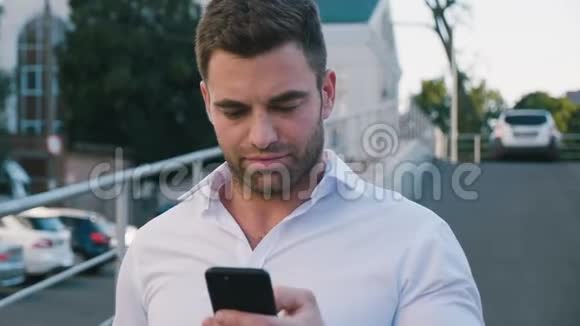 在办公楼附近的停车场散步的商人画像看着他的智能手机屏幕白色衬衫视频的预览图