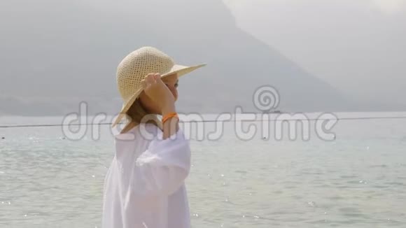 海山背景上戴草帽的少女雾蒙蒙在绿色沙滩上摆姿势的快乐少女视频的预览图