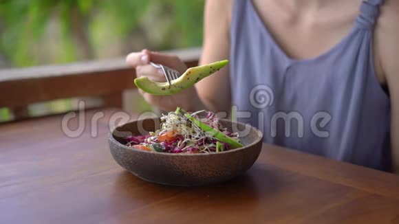 一个在热带咖啡馆里的年轻女人吃健康的素食沙拉素食概念慢镜头视频的预览图