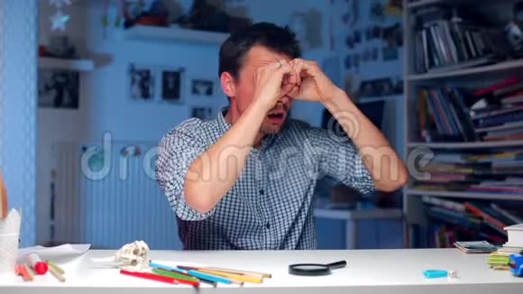 一个男人坐在办公室的一张桌子旁用双手抱着眼睛看着视频的预览图