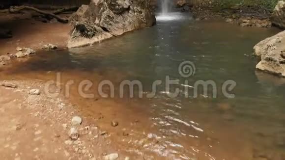 一位背着背包的男性旅行者在森林中一个雄伟的瀑布前爬上悬崖视频的预览图