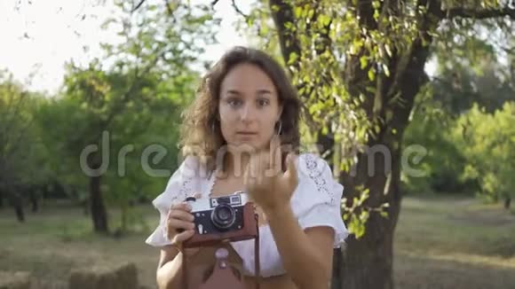 可爱的年轻摄影师的肖像卷发一边看着相机一边用旧相机拍照视频的预览图