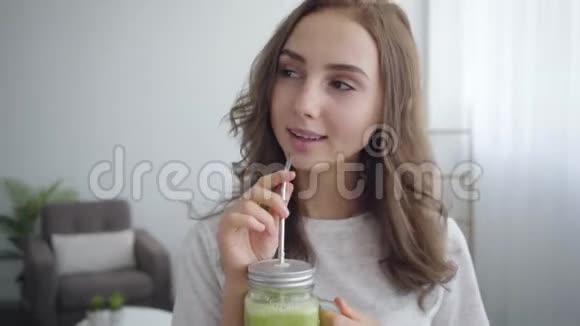 年轻苗条的女人在家里厨房的小罐子里喝着美味的冰沙健康食品的概念职业视频的预览图
