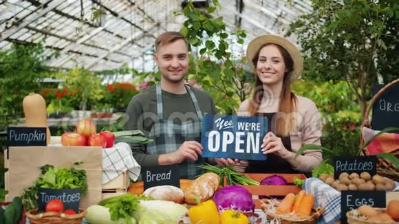 男人和女人拿着开放标志站在餐桌前摆着市场上的有机食品视频的预览图