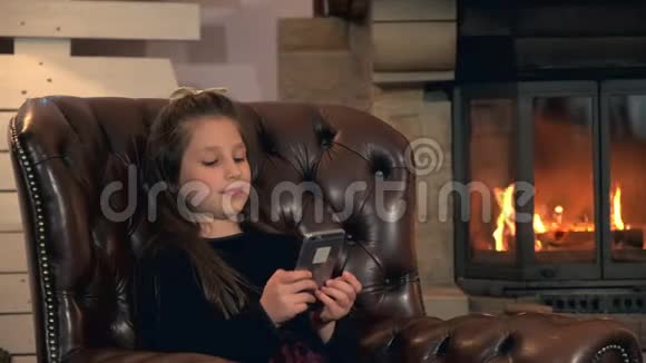 小女孩在壁炉旁用智能手机打发闲暇时间视频的预览图