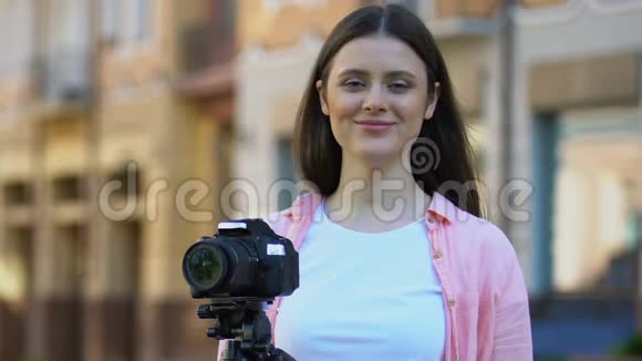 快乐的女摄影师在三脚架上的相机附近创造性的工作博客爱好视频的预览图