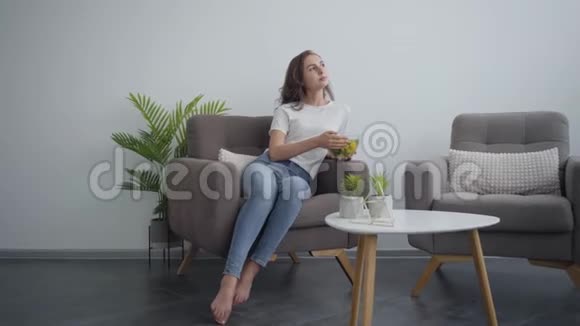 年轻苗条的女人拿着大碗和沙拉一边坐在扶手椅上享受健康的食物健康生活方式视频的预览图