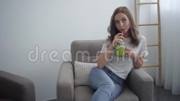 漂亮的年轻女人在家里厨房的小罐子里喝着美味的冰沙健康食品的概念视频的预览图