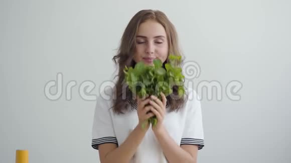 年轻漂亮的女人嗅着站在现代厨房餐桌前的新鲜绿色健康食品的概念职业视频的预览图