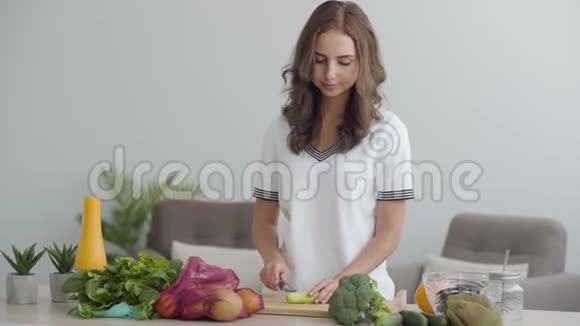 年轻苗条的女人用锋利的刀在厨房的桌子上切蔬菜健康食品的概念许多视频的预览图