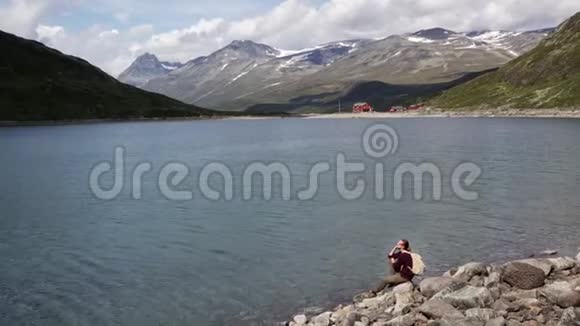 年轻的女旅行者坐在岩石上欣赏山湖美景视频的预览图
