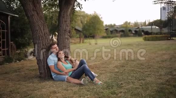 一对浪漫的夫妇坐在一棵双树下一个女孩在一个男人的大腿上一对相爱的夫妇在草地上的公园里休息视频的预览图