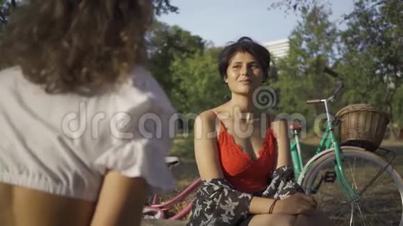 两个可爱的女人在夏天的花园里坐在一起说话她们的自行车站在附近农村生活复古视频的预览图