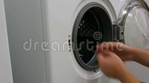 男人把衣服和衣服装进洗衣机洗衣房内大型白色洗衣机视频的预览图