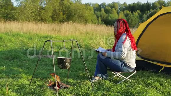 一个靠近火边头巾的女人读一本书看一个沸腾的锅视频的预览图