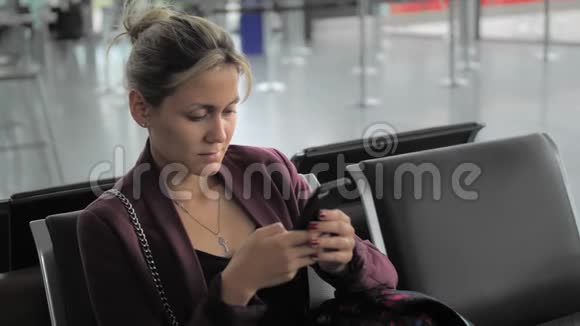 漂亮的白种人女性在智能手机上打字而坐在机场航站楼乌尔巴和快乐这就是视频的预览图