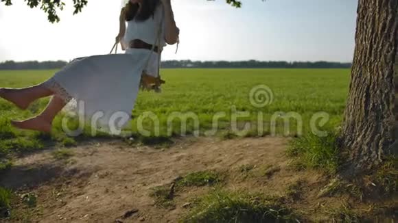 年轻的赤脚女孩穿着一件美丽的白色乡村连衣裙在开阔的田野上荡秋千视频的预览图