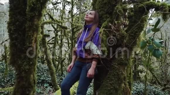 在一片神秘的森林里一个女孩靠在长满苔藓的树上视频的预览图