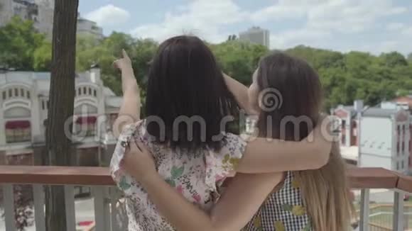 两个漂亮的女孩站在户外拥抱和交谈欣赏美丽的城市景观女朋友在讨论视频的预览图