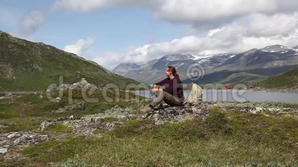 年轻的女旅行者坐在岩石上从瓶子里喝水视频的预览图