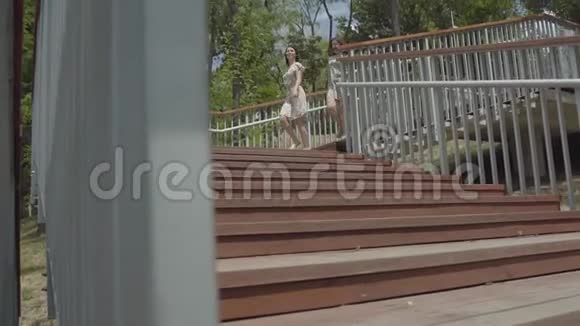 两个穿着夏装的可爱的年轻在城市公园的楼梯上奔跑无忧无虑的女朋友玩得开心视频的预览图