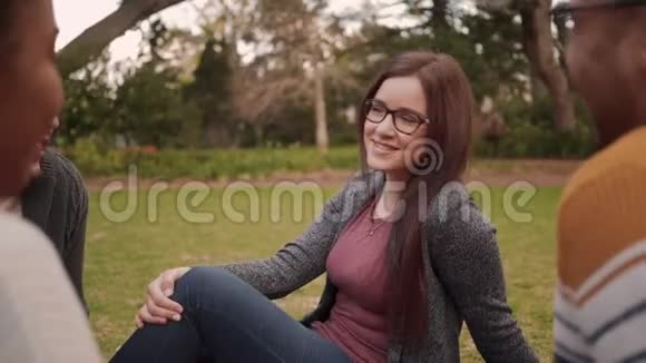 一位美丽的微笑的年轻女子和她的多民族朋友坐在一起在公园里享受的肖像视频的预览图