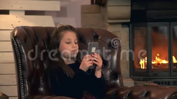 在壁炉旁的智能手机上玩游戏的小漂亮女孩视频的预览图