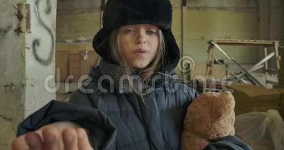 一个无家可归的白人女孩穿着肮脏的冬天衣服抱着泰迪熊要求施舍的肖像饥饿视频的预览图