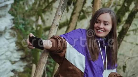 一个可爱的女孩在一片雾蒙蒙的木林中长满苔藓的树木的背景下做一个和平的自我视频的预览图