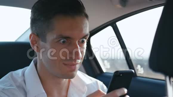 商人在智能手机上读一条好消息他快乐而微笑男人和司机或出租车一起开车视频的预览图