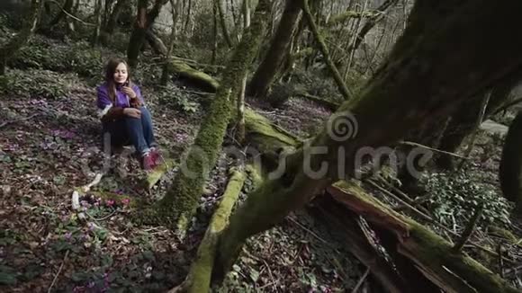 美丽的女孩坐在童话森林里看着手中的花朵视频的预览图