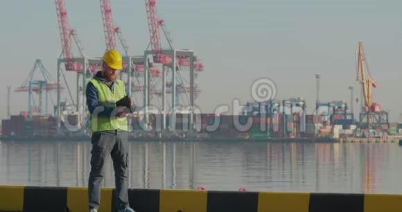 一个黄盔架上有一颗胡子的码头工人在码头上有一台平板电脑背景是起重机和集装箱这就是视频的预览图