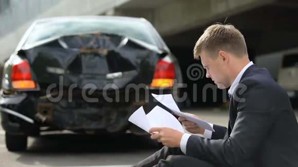 车祸后男司机坐在路上看保险合同视频的预览图