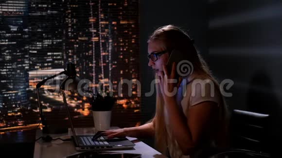 年轻的女经理在电脑上工作用智能手机和别人说话视频的预览图