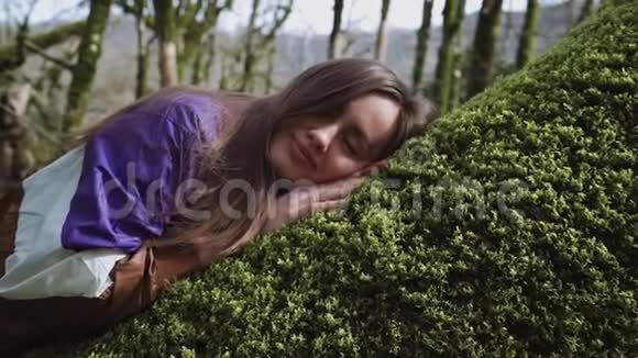 穿紫色夹克的漂亮女孩睡在森林中央的绿苔上视频的预览图