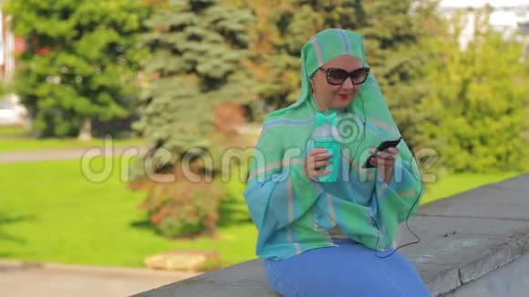 公园里一位年轻活泼的穆斯林妇女戴着一条浅色围巾和太阳镜喝着咖啡在送信的时候和他交谈视频的预览图