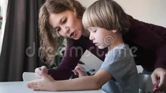 小男孩坐在家里的桌子上和他们的妈妈一起画画家庭概念视频的预览图