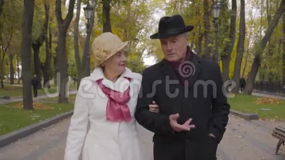 在秋天公园散步的一对高加索族夫妇的特写镜头穿着黑色外套和帽子的成熟男人和他说话视频的预览图