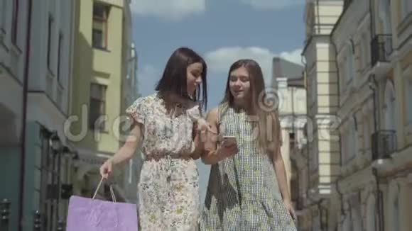 两个可爱的女朋友在美丽的建筑前用购物袋购物后正在谈论新闻视频的预览图