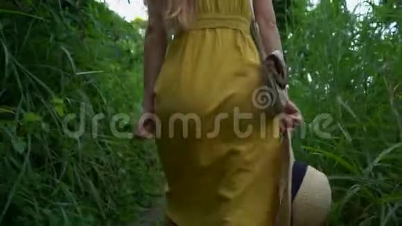 一位穿着黄色连衣裙的年轻女子在坎布汉岭散步或画家乌布的人行道上散步旅行目的地视频的预览图