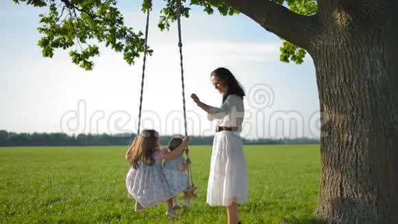 可爱的妈妈在一棵老树上绑着的绳子秋千上摆动她的女儿视频的预览图