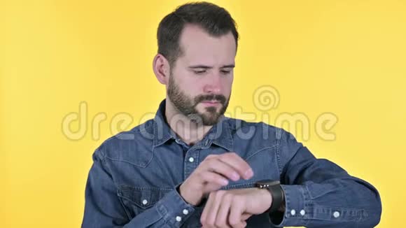 职业胡子青年使用智能手表黄色背景视频的预览图