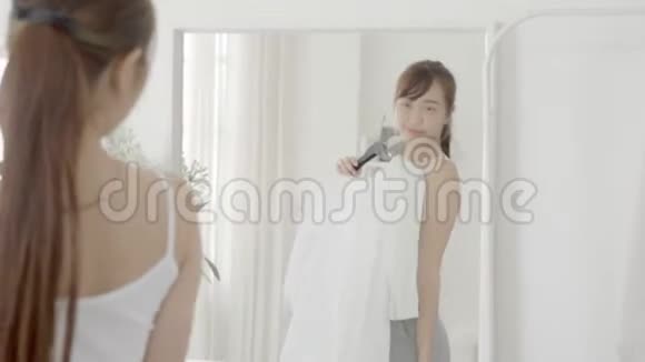 美丽的肖像亚洲年轻女子微笑着在卧室照镜子亚洲女孩试着穿衣服视频的预览图