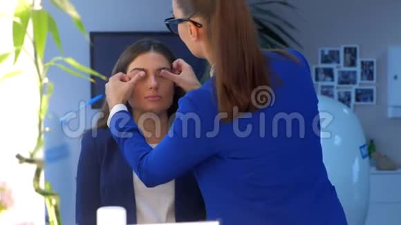 化妆师在沙龙中将基色调霜涂在女孩眼皮上摩擦手指视频的预览图