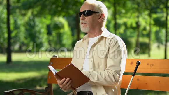 戴黑墨镜的盲人厌倦了阅读盲文书籍坐在公园里视频的预览图