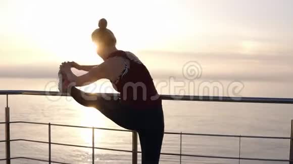 慢镜头集中运动年轻女子伸展腿在木制码头与金属栅栏美丽的金发美女视频的预览图