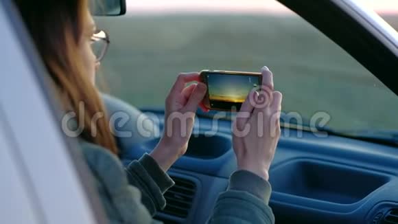 戴眼镜的女孩从车里拍日落照片视频的预览图