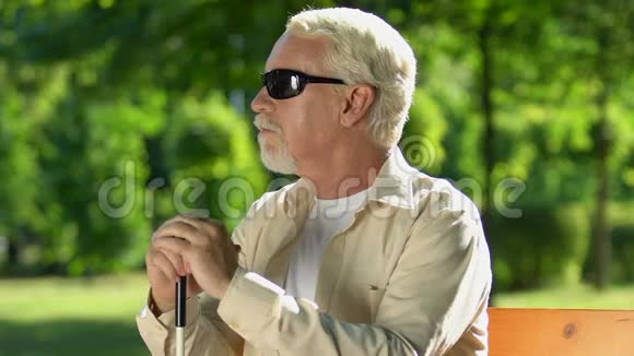 有视力问题的老人坐在公园的长椅上享受大自然和空气视频的预览图